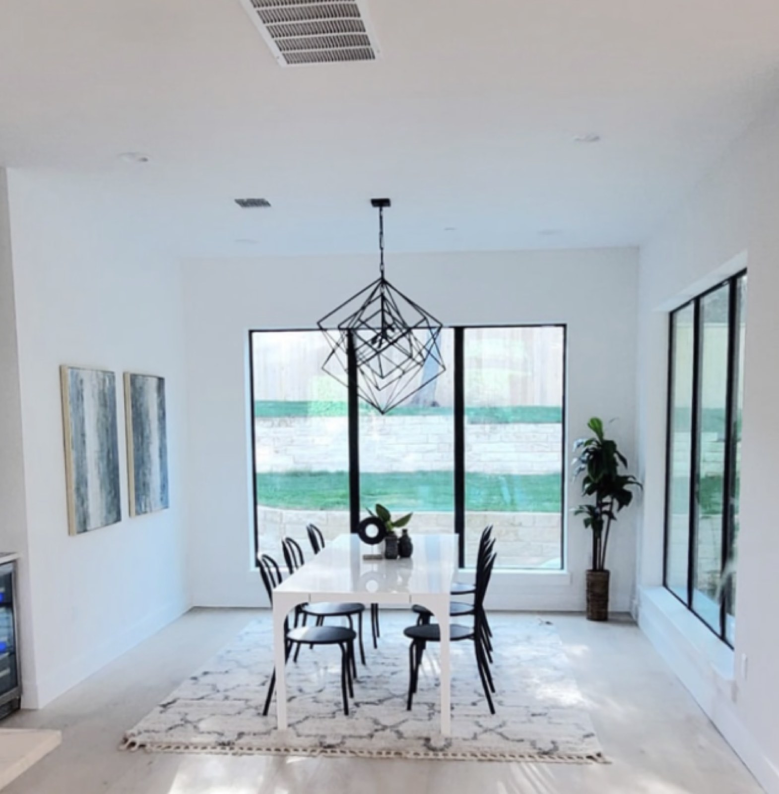 Bright white dining room with floor to ceiling black steel windows and a geometric chandelier