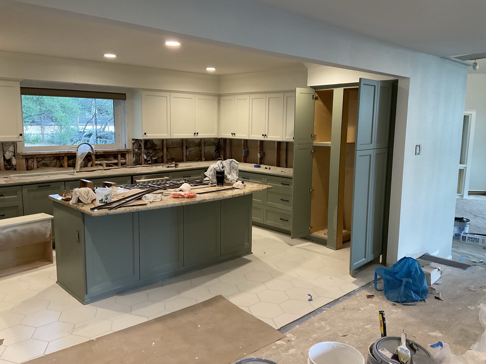 The same kitchen mid-project: cabinet doors removed, sage green paint going on the island and lower cabinets